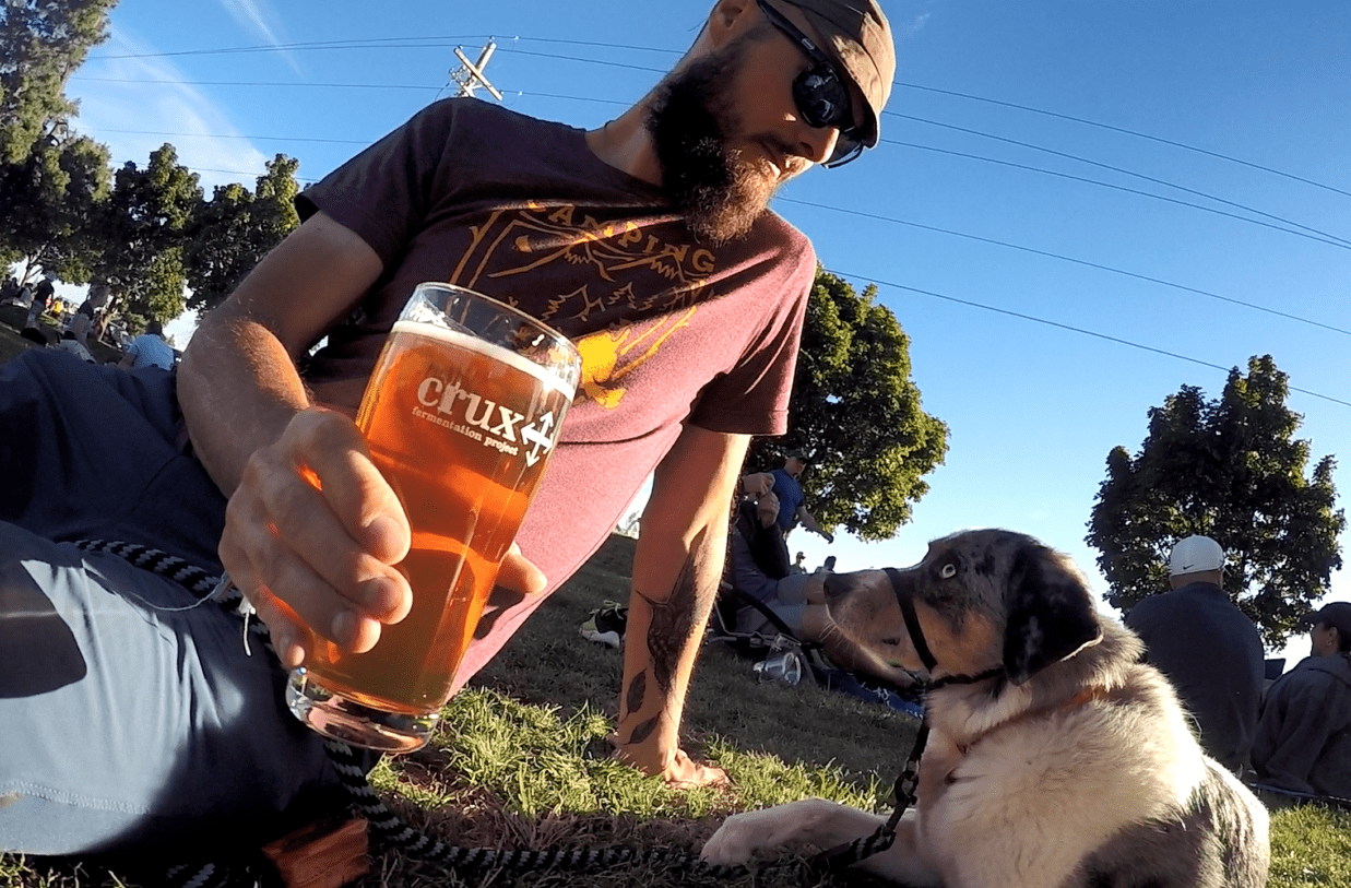 Man and dog sitting on the grass with a glass of kombucha at the pet-friendly restaurant, Kebaba, in Bend, Oregon
